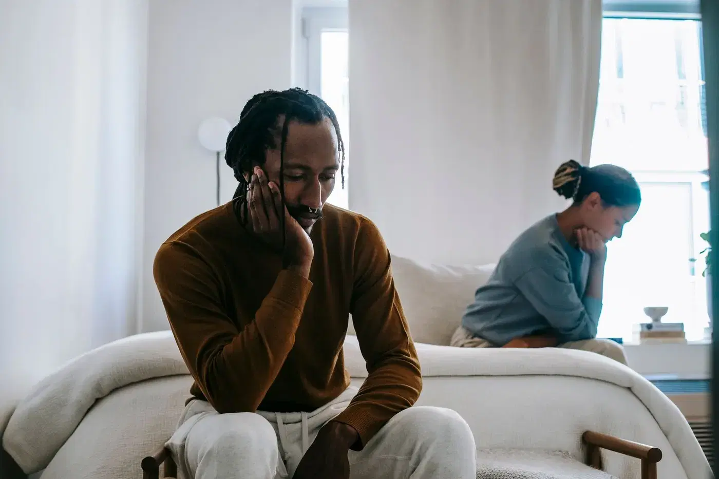 A man resting his head in his hand while his partner sits turned away behind him