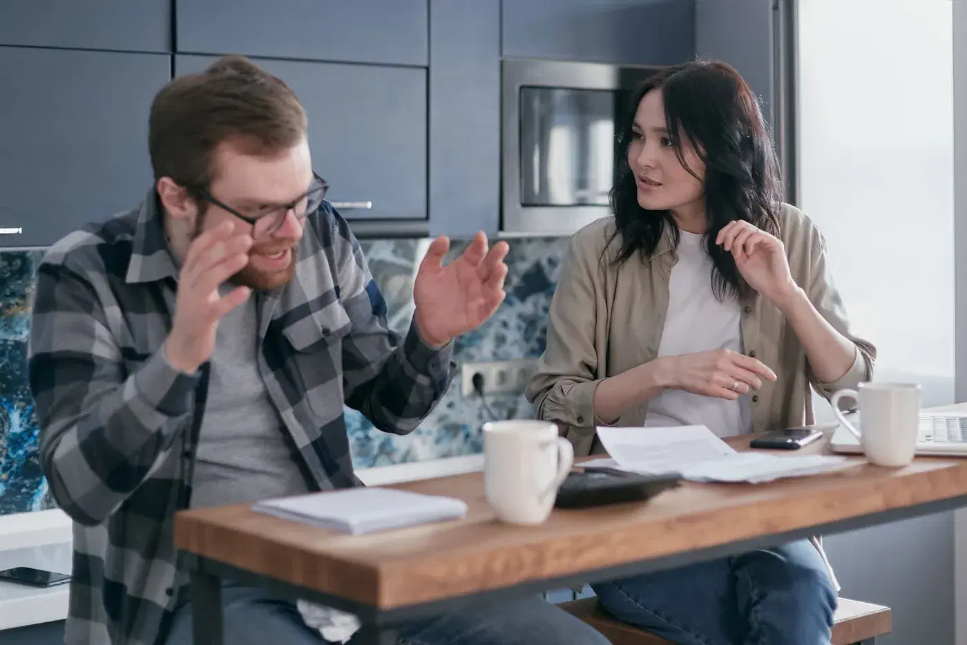 A man explaining with open hands while the woman beside him listens at a kitchen table