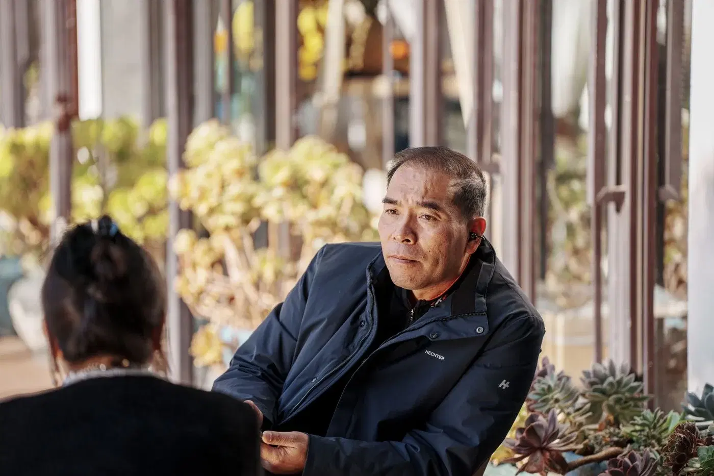 A man listening closely to the person sitting across from him at an outdoor table