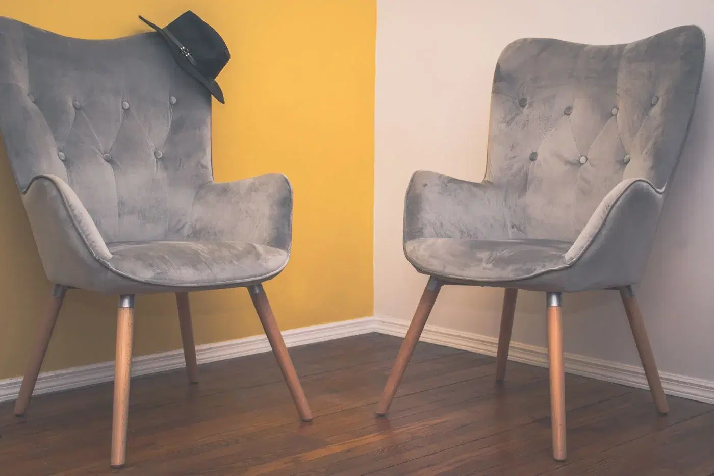 Two grey armchairs side by side in a plain room with a yellow wall