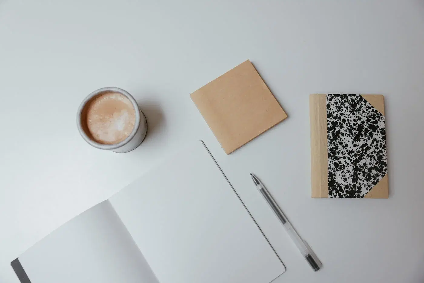Two notebooks, a pen and a cup of coffee arranged on a white surface