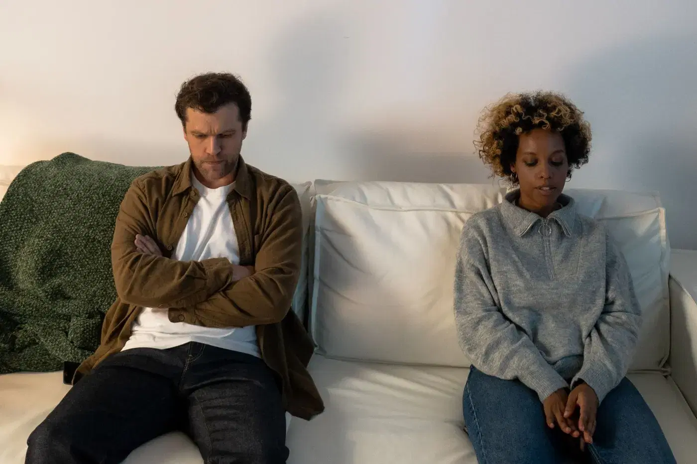 A man and a woman sitting at opposite ends of a sofa, not looking at each other