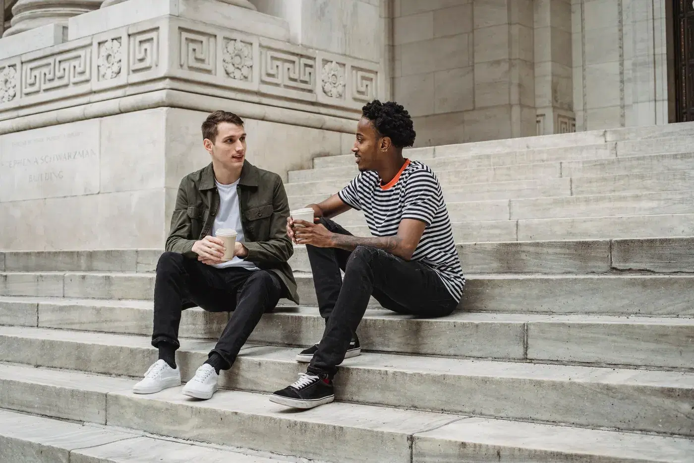 Two friends sitting on stone steps outdoors, talking